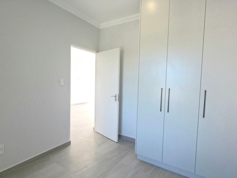 A clean, empty bedroom featuring neutral tiled flooring, built-in cupboards, and a doorway leading to an adjacent room.