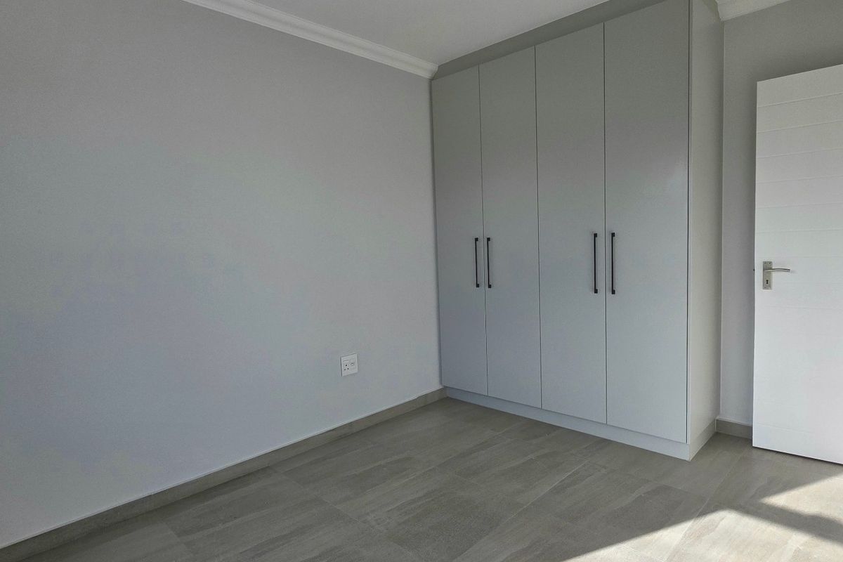 A clean, modern bedroom featuring neutral grey walls, light-toned tiled flooring, and ample built-in cupboard storage.