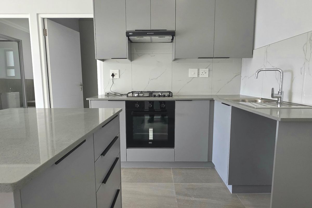 Modern kitchen featuring grey cabinetry, stone countertops, a central island, and integrated appliances including a gas hob and oven.