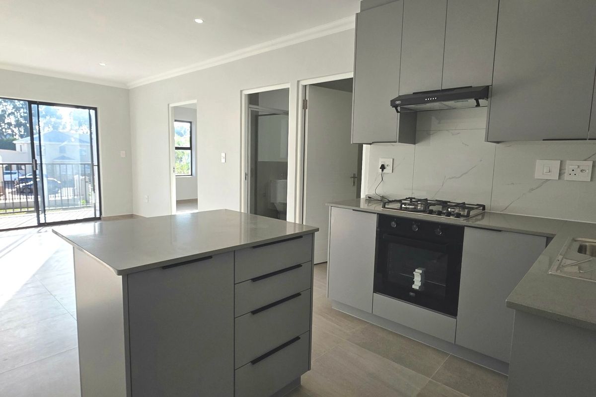 Modern open-plan living area featuring a sleek kitchen with stone countertops, built-in appliances, and large sliding doors leading to an outdoor space.
