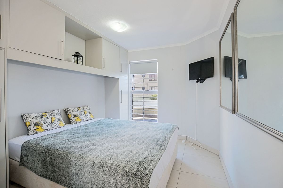 A bedroom featuring built-in overhead cabinetry, tiled flooring, and a window with security bars.