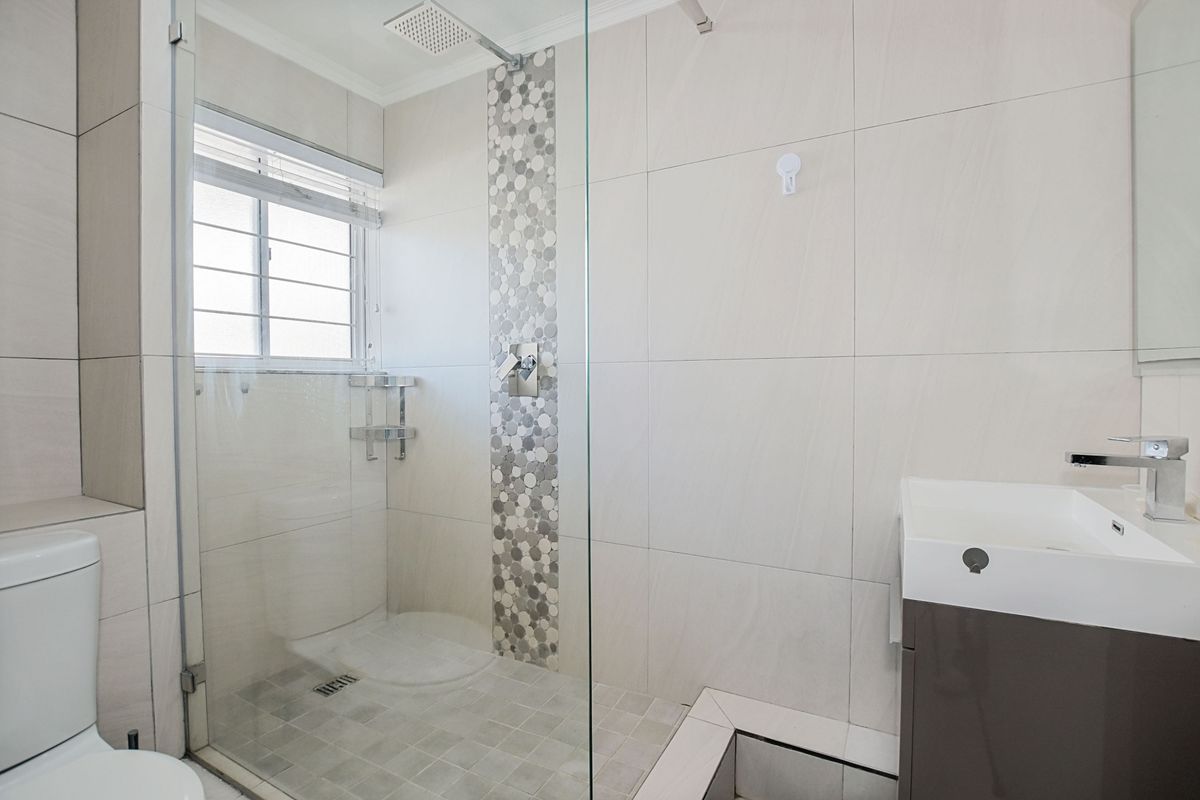 Modern bathroom featuring a glass-enclosed walk-in shower with mosaic tile accents, a contemporary vanity, and neutral wall tiling.
