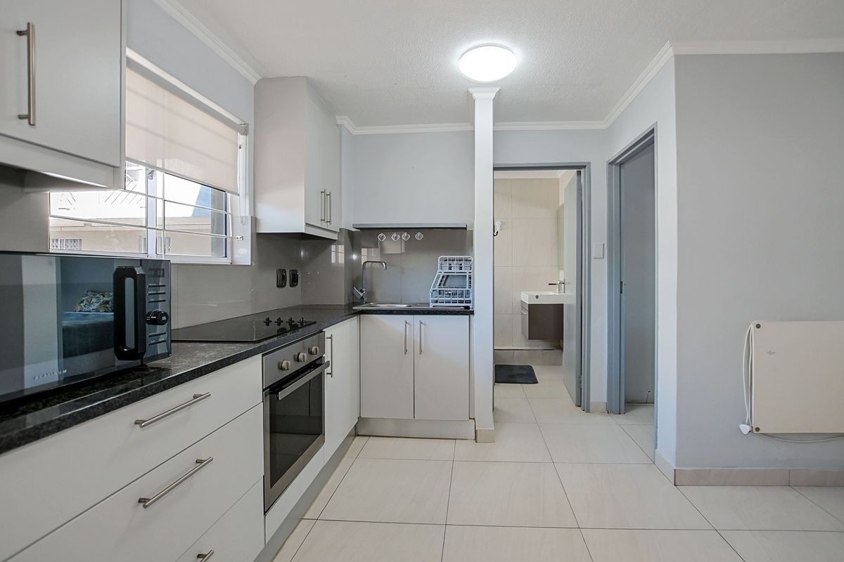 A clean, modern kitchen featuring white cabinetry, dark stone countertops, a built-in oven, and a hob, with direct access to an adjacent bathroom.