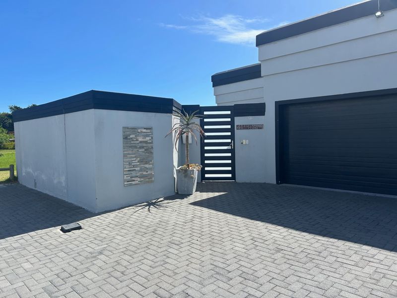 Front exterior view of the property featuring a paved driveway, modern garage door, and a secure pedestrian gate entrance.