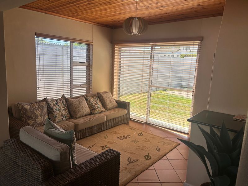A cozy living room featuring a warm timber-clad ceiling, tiled flooring, and large sliding glass doors that provide direct access to the garden.