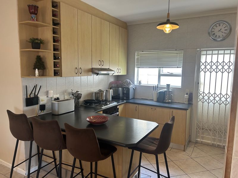 Functional kitchen featuring light wood cabinetry, dark countertops, a breakfast bar, built-in gas hob, and an integrated extractor fan.