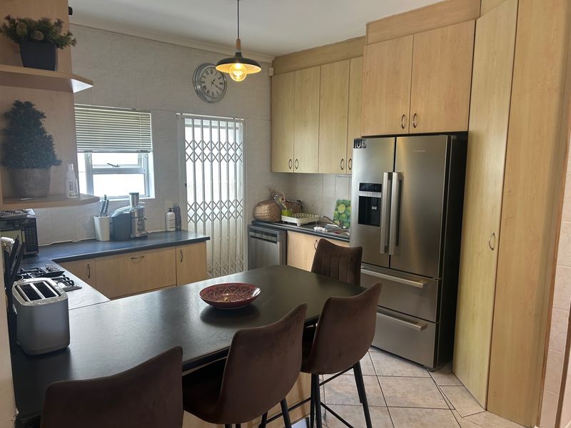 A functional kitchen featuring light wood cabinetry, dark countertops, tiled flooring, and a breakfast bar area with integrated appliance space.