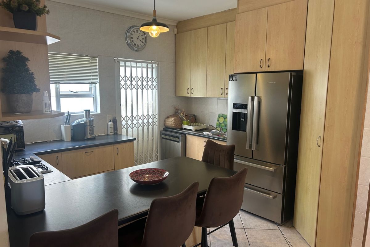 A functional kitchen featuring light wood cabinetry, dark countertops, tiled flooring, and a breakfast bar area with integrated appliance space.