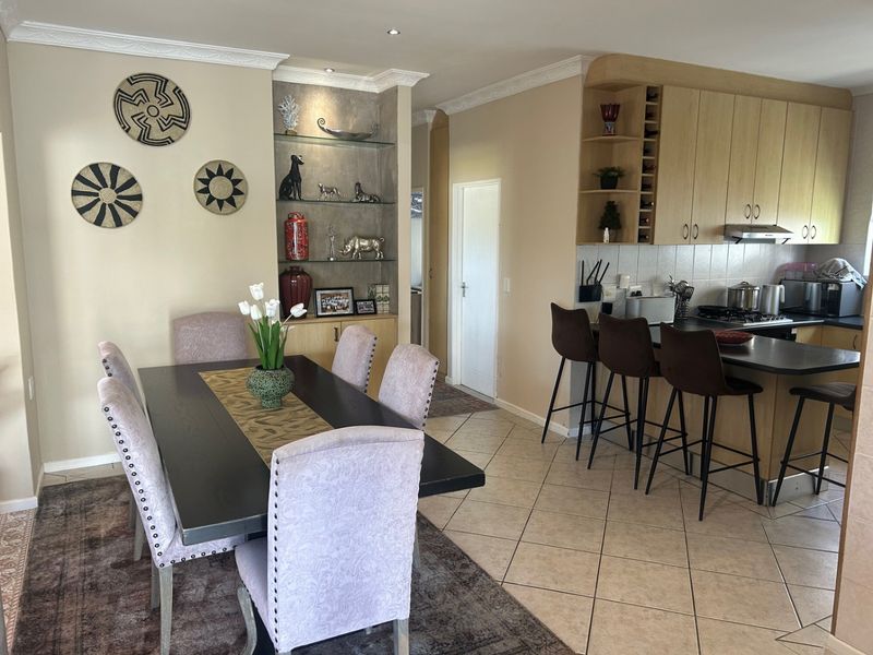 Open plan dining and kitchen area featuring light wood cabinetry, a breakfast bar, tiled flooring, and built-in display shelving.