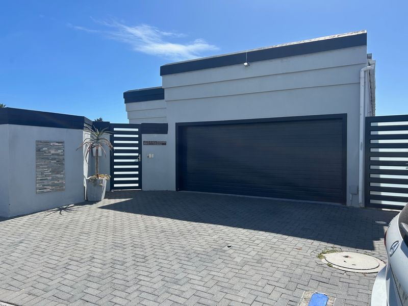 Modern exterior front view of the property featuring a paved driveway, a large dark garage door, and contemporary boundary wall detailing.