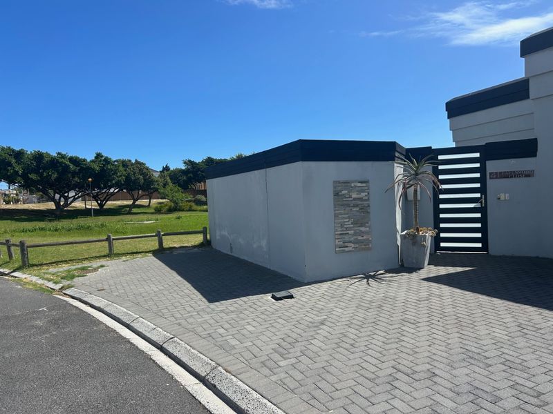 Front exterior view of the property featuring a paved driveway, modern boundary wall with stone cladding detail, and a secure gated entrance.