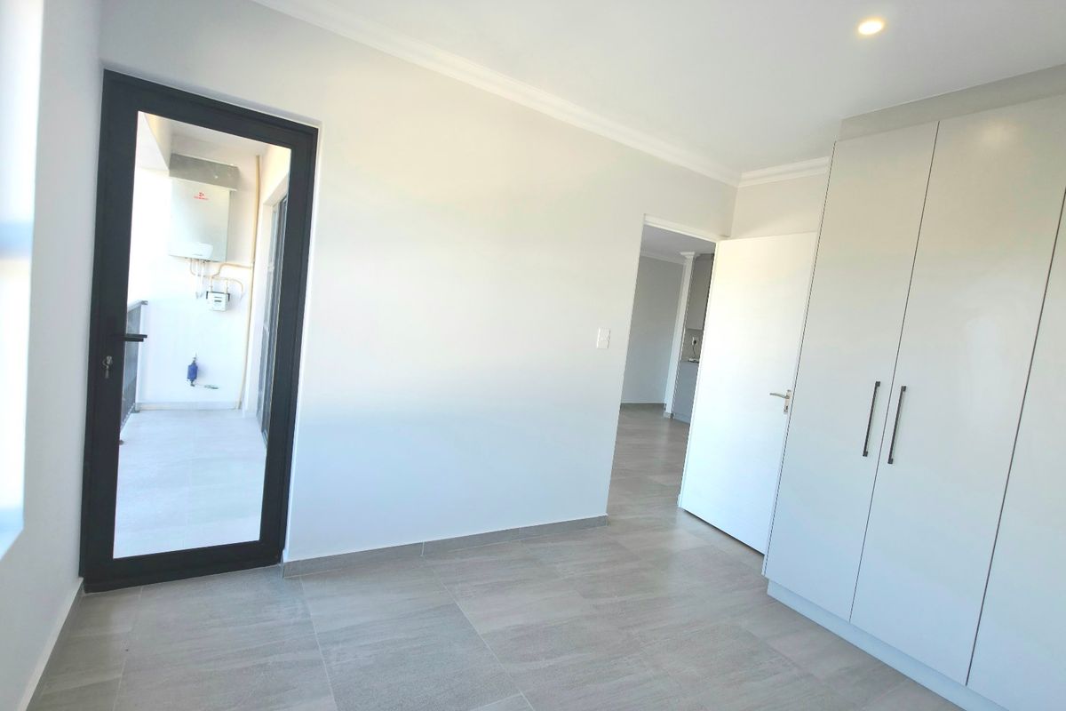 A bright, modern bedroom featuring neutral tiled flooring, built-in cupboards, and direct access to an outdoor balcony area.