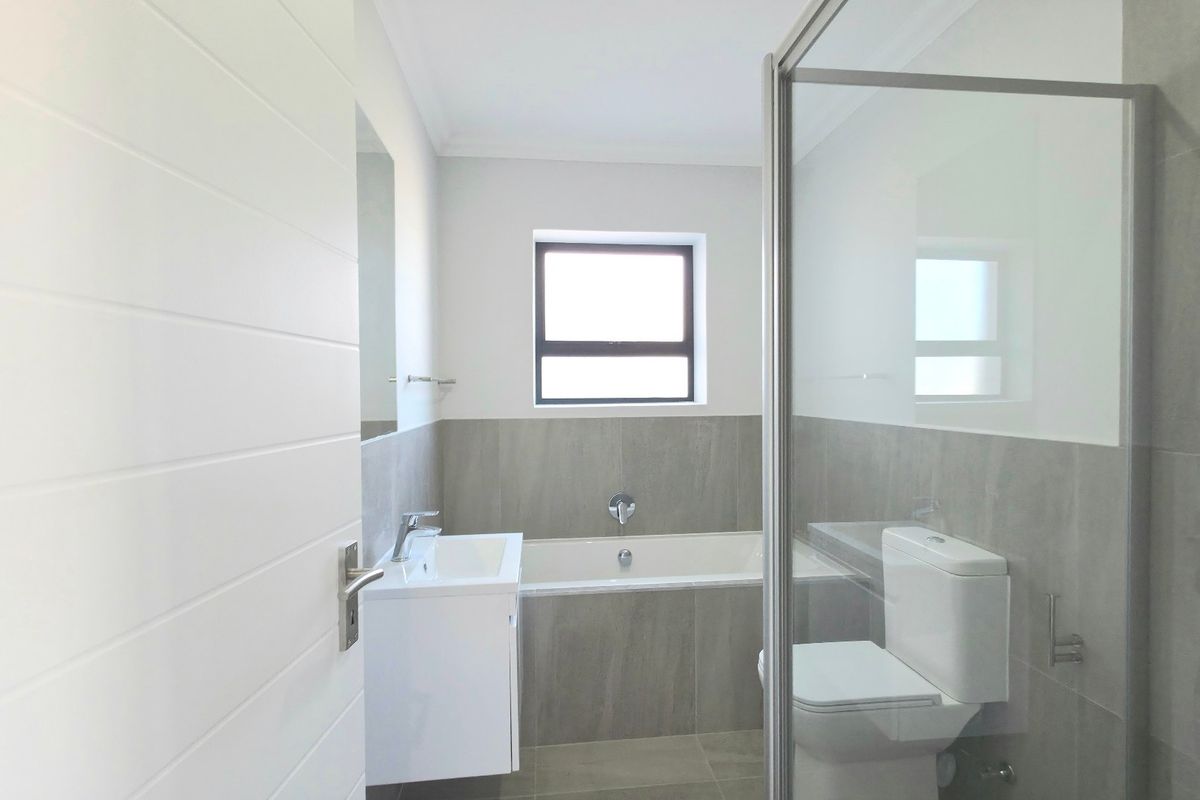 A modern, clean bathroom featuring a built-in vanity, a bathtub, a separate shower enclosure, and neutral grey tiling throughout.