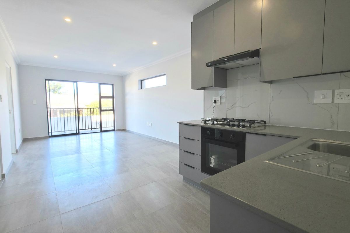 Modern open-plan living area featuring a sleek kitchen with stone countertops, gas hob, and integrated appliances, leading to a bright balcony through sliding doors.