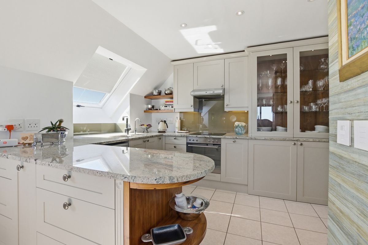 Modern kitchen featuring granite countertops, shaker-style cabinetry, integrated oven and hob, and a skylight window providing ample natural light.