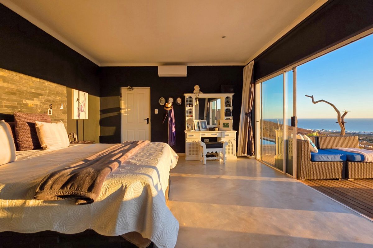 Spacious bedroom featuring a stone accent wall, polished concrete floors, and large sliding glass doors opening onto a deck with ocean views.