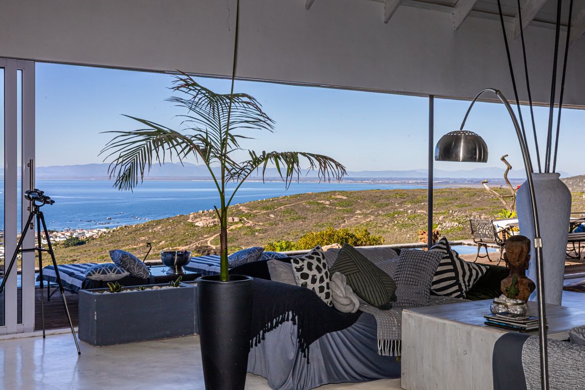 Spacious living area featuring polished concrete floors and exposed timber rafters, opening onto a deck with expansive coastal and ocean views.