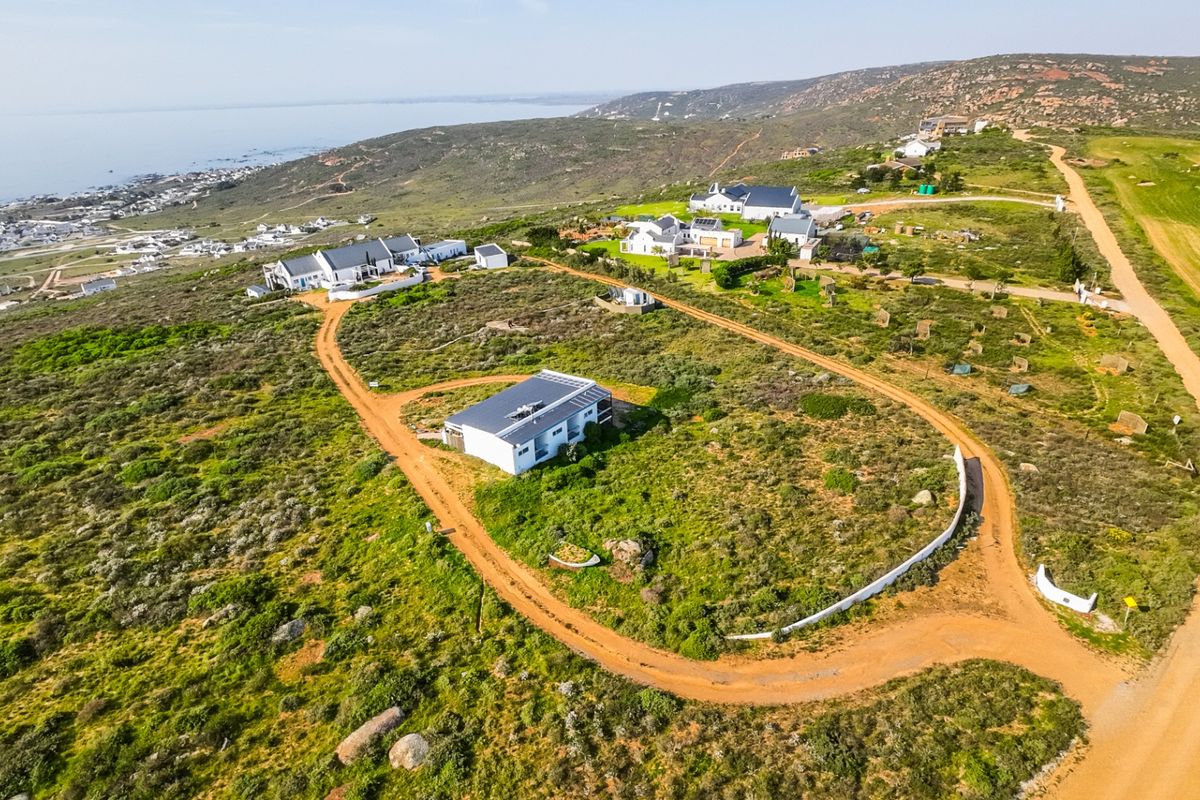 Aerial view of a coastal property featuring a modern home with solar panels, surrounded by natural landscape and gravel access roads.