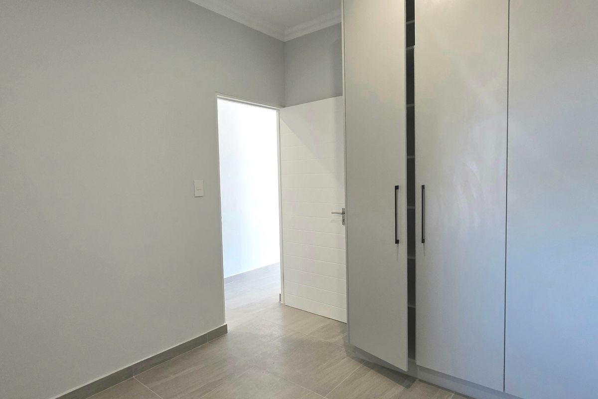 A clean, empty bedroom featuring neutral tiled flooring and modern built-in cupboards with sleek handles.