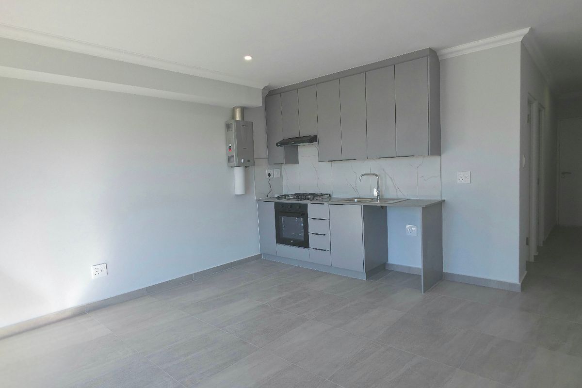 Modern open-plan kitchen featuring grey cabinetry, built-in gas hob, electric oven, extractor fan, and tiled flooring in a clean, neutral space.