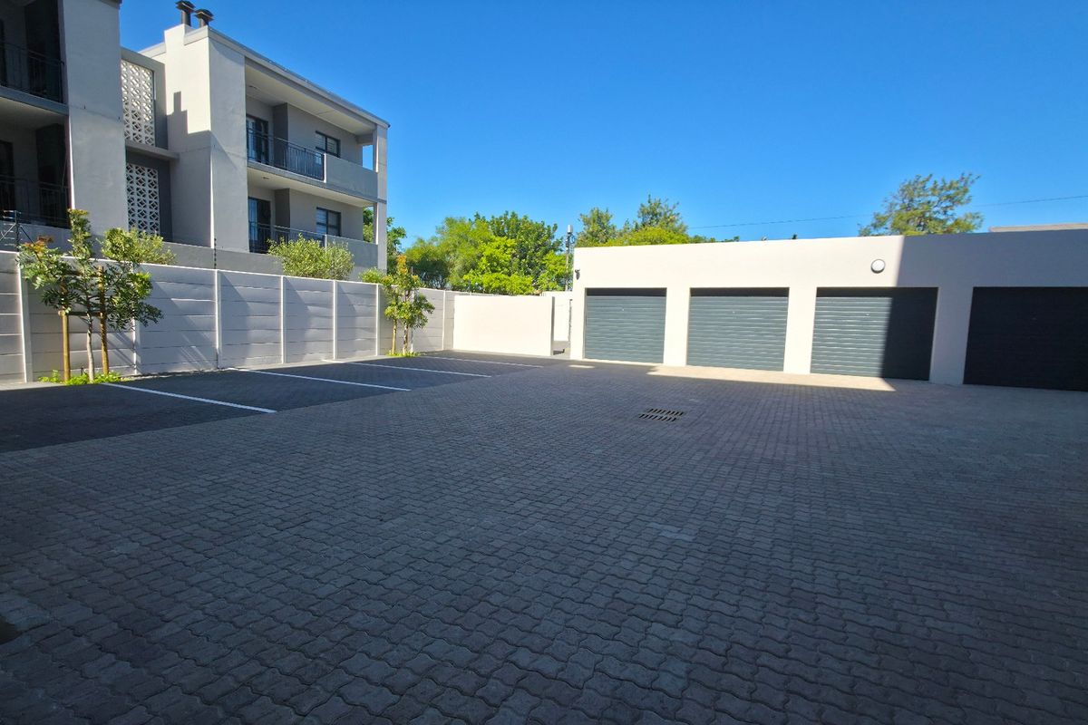 A well-maintained paved parking area featuring three secure garage units and a clean concrete boundary wall within an apartment complex.