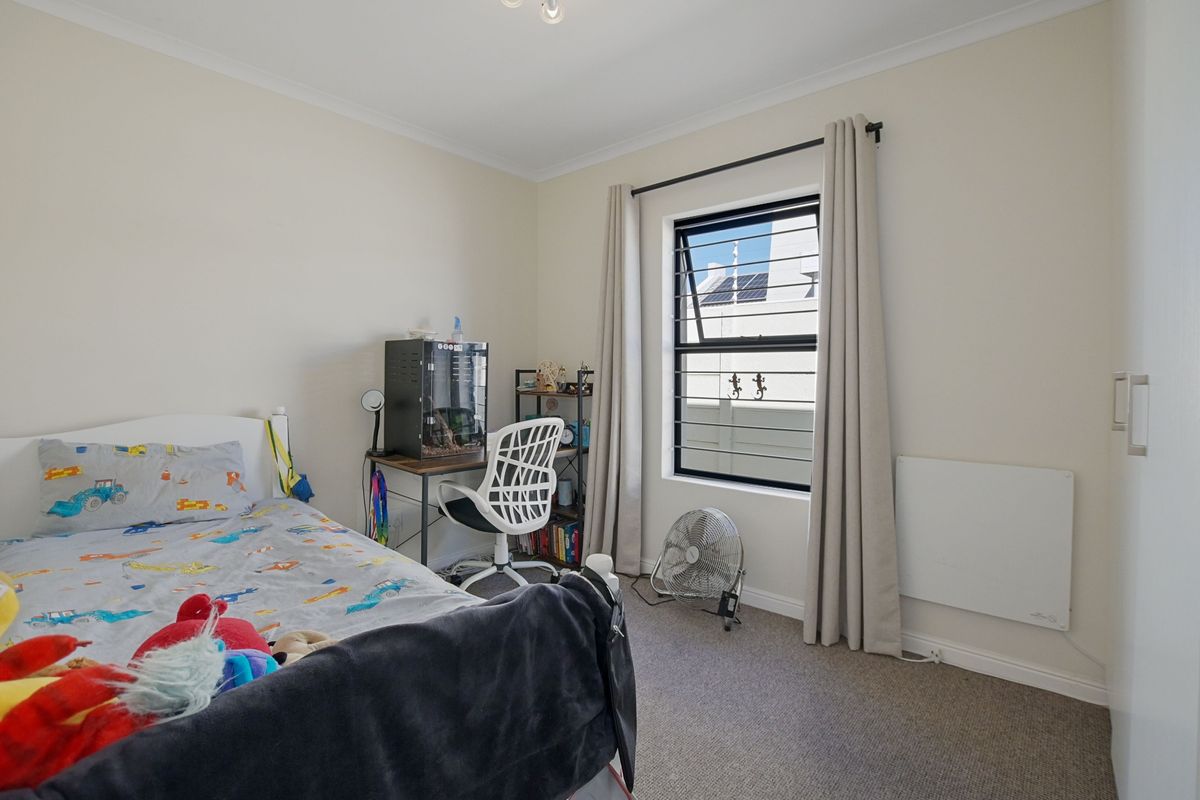 A functional bedroom featuring neutral carpeting, a window with security bars, and a wall-mounted panel heater.