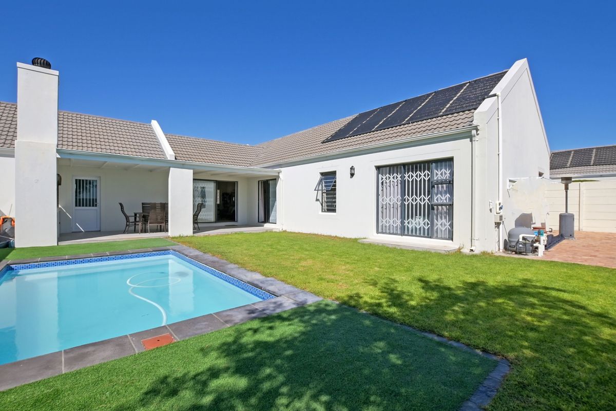 Rear view of the property featuring a swimming pool, covered patio area, lawn, and roof-mounted solar panels.