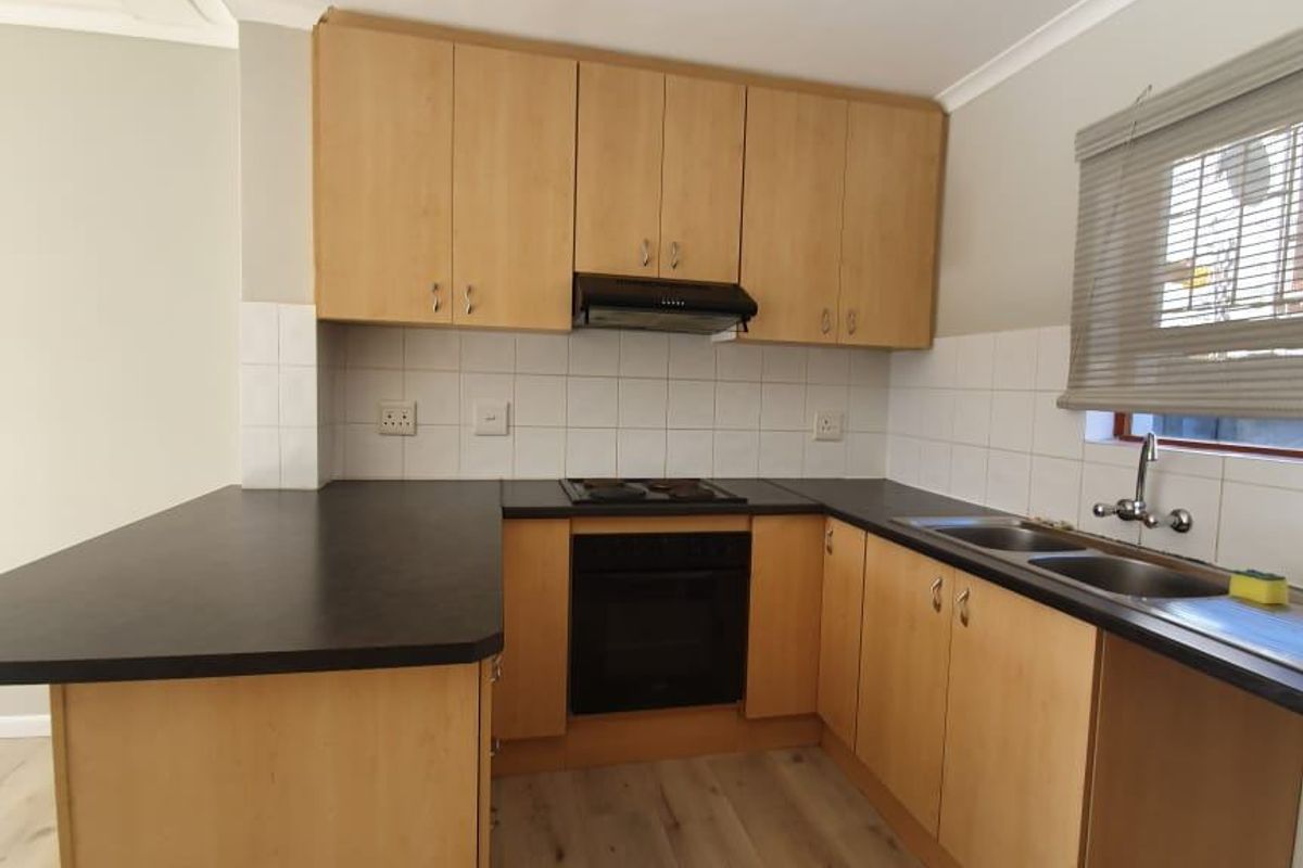 A functional kitchen featuring light wood cabinetry, dark laminate countertops, a built-in oven, hob, extractor fan, and a double stainless steel sink.