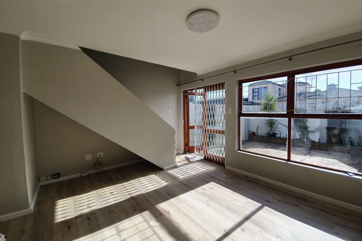 Bright living area featuring wood-look laminate flooring, large windows with security bars, and a staircase with under-stair storage space.