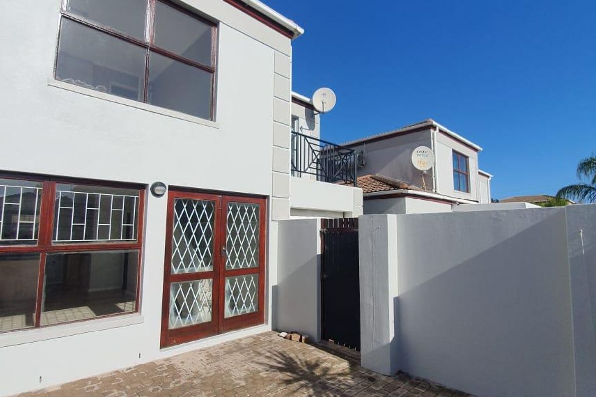 A rear exterior view of a townhouse featuring a paved courtyard, security gates, and a balcony on the upper level.