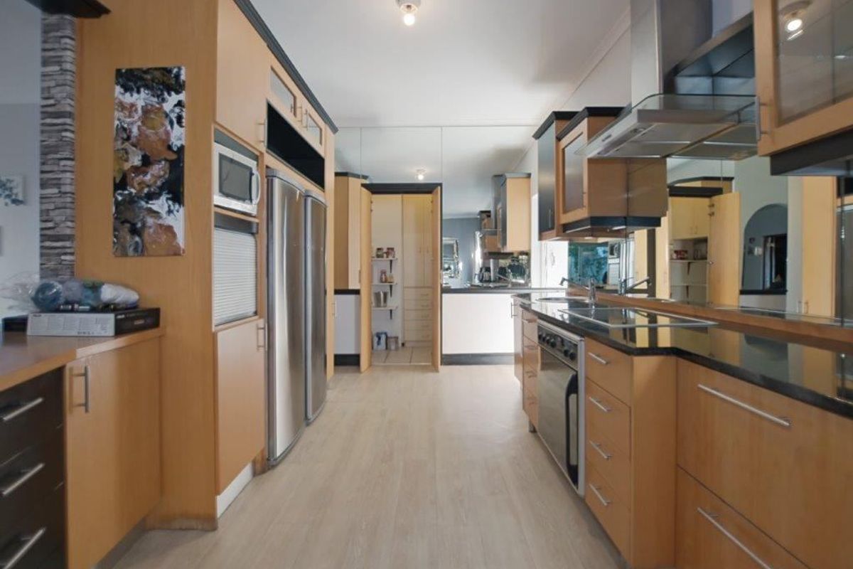A functional kitchen featuring light wood cabinetry, dark granite countertops, stainless steel appliances, and a convenient adjoining scullery area.