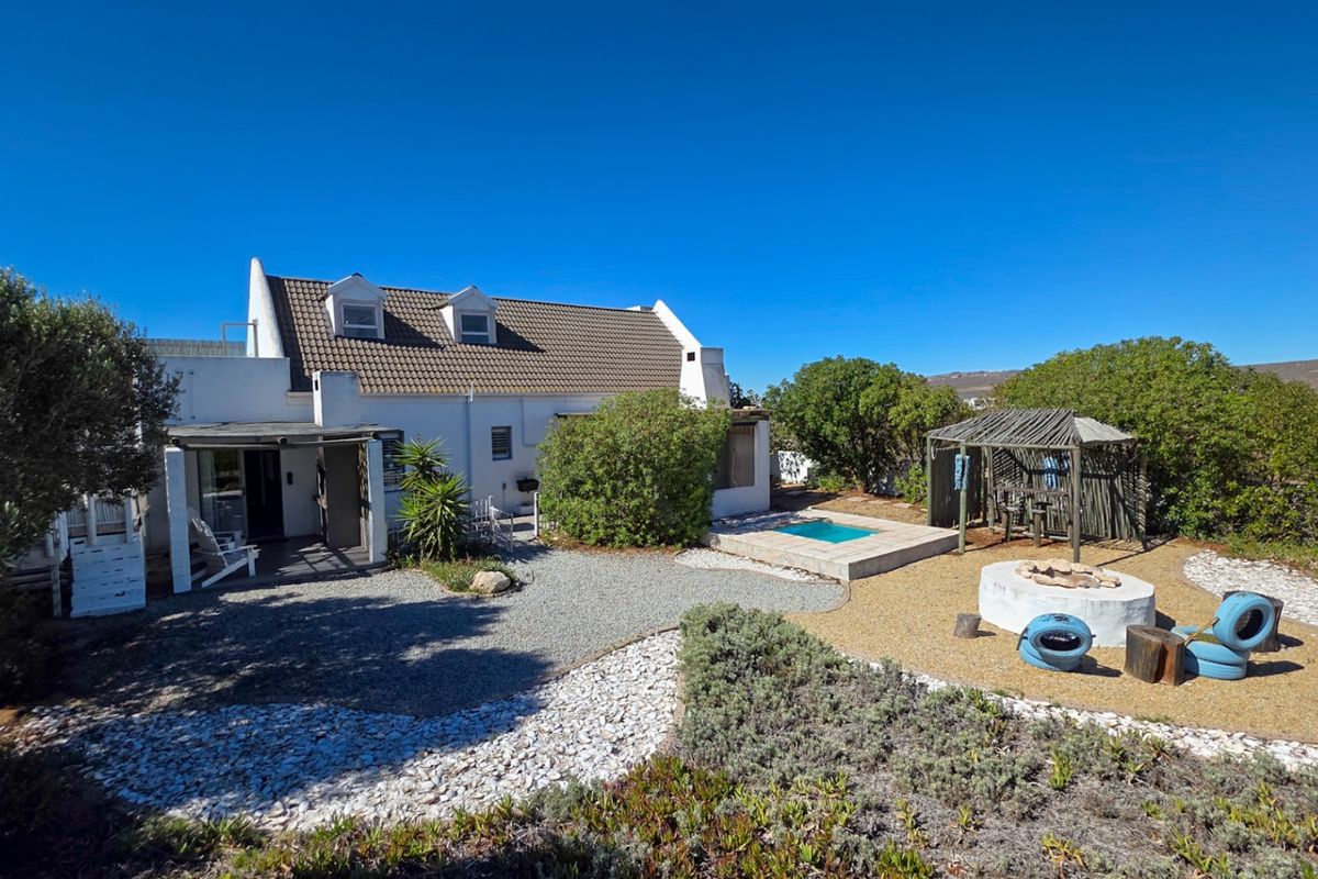 Rear view of the property featuring a white cottage-style house, a small swimming pool, a covered patio area, and a fire pit in the garden.