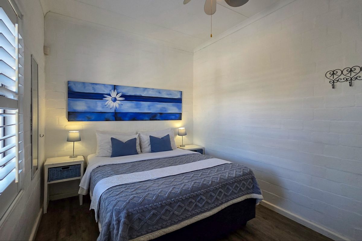 A well-maintained bedroom featuring white painted brick walls, timber-look flooring, and plantation shutters.