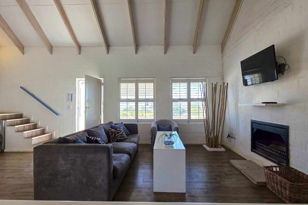 Spacious living room featuring vaulted ceilings with exposed timber beams, a built-in fireplace, and plantation shutters, creating a bright and airy atmosphere.