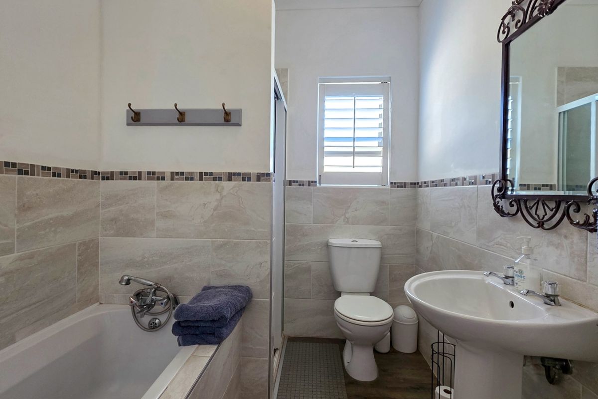 A well-maintained bathroom featuring a bathtub, pedestal sink, toilet, and neutral wall tiling with a decorative mosaic border.