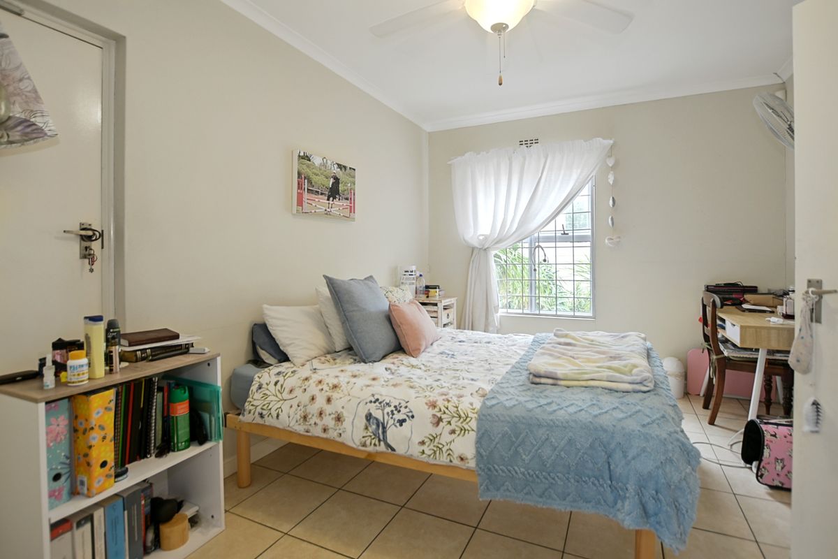 A functional bedroom featuring tiled flooring, a ceiling fan, and a window with security bars, providing a comfortable living space.