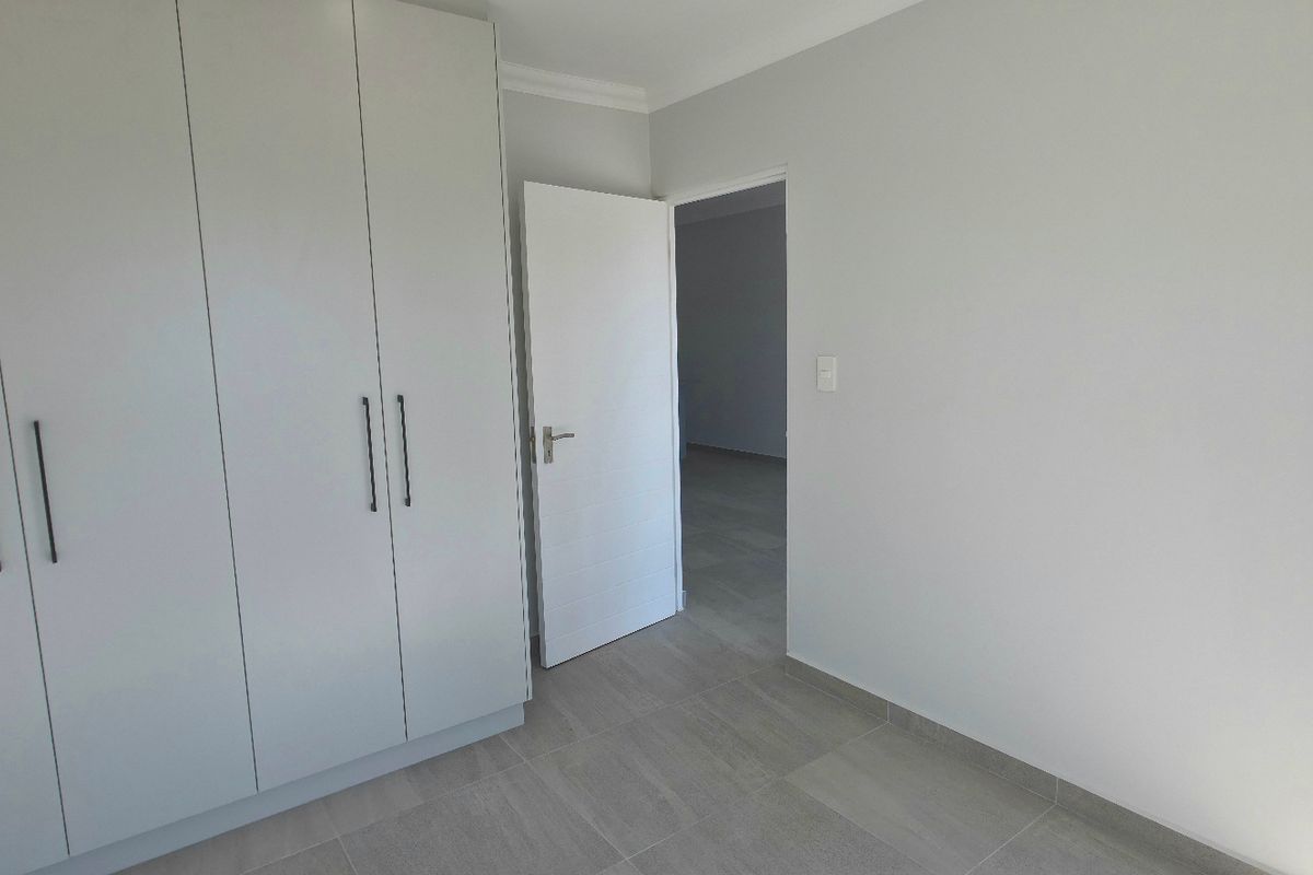 A bright bedroom featuring built-in cupboards, neutral tiled flooring, and direct access to an outdoor area through a glass door.