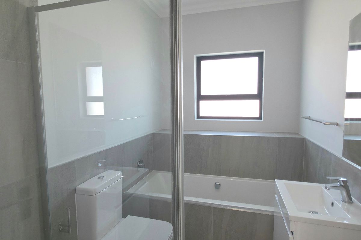Modern bathroom featuring a glass-enclosed shower, a built-in bathtub, a vanity basin, and neutral grey wall tiling.
