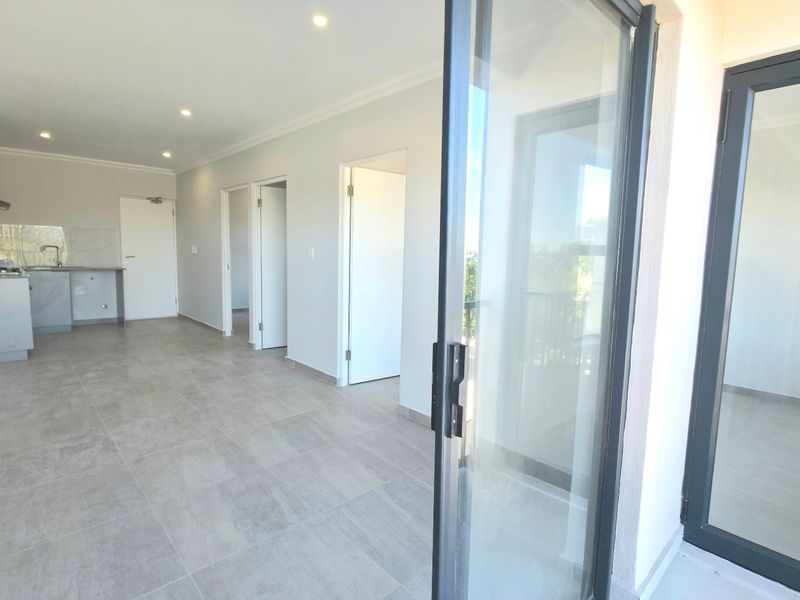 Spacious open-plan living area featuring modern tiled flooring, recessed lighting, and a sleek kitchen with built-in cabinetry, leading to a balcony through sliding doors.