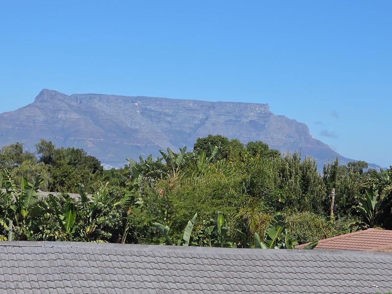 A clear, elevated view of Table Mountain overlooking surrounding lush greenery and residential rooftops.