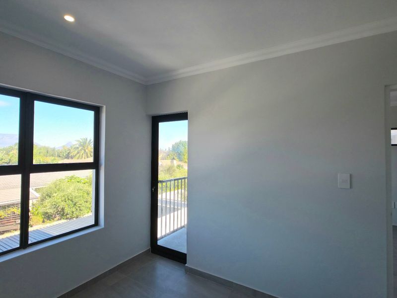 A bright, empty bedroom featuring modern tiled floors, recessed lighting, and direct access to a private balcony through an aluminium-framed door.