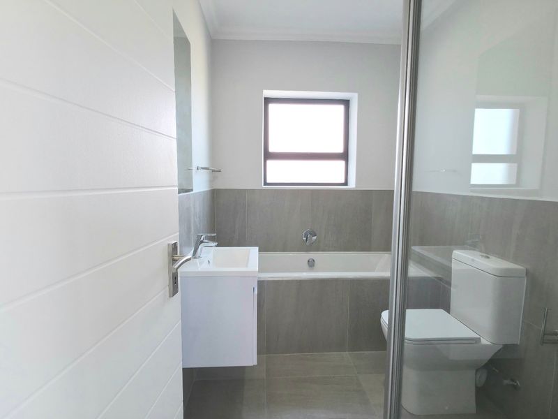 Modern bathroom featuring a built-in bathtub, wall-mounted vanity, toilet, and a glass-enclosed shower with neutral grey tiling throughout.