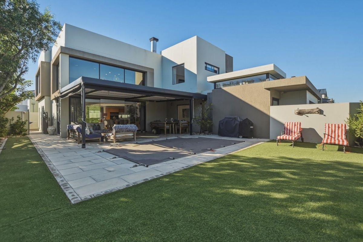 Modern rear exterior featuring a covered patio, paved terrace, swimming pool with safety cover, and landscaped garden area.