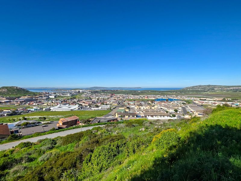 A wide-angle elevated view overlooking the surrounding residential neighborhood, coastal landscape, and distant hills under a clear blue sky.