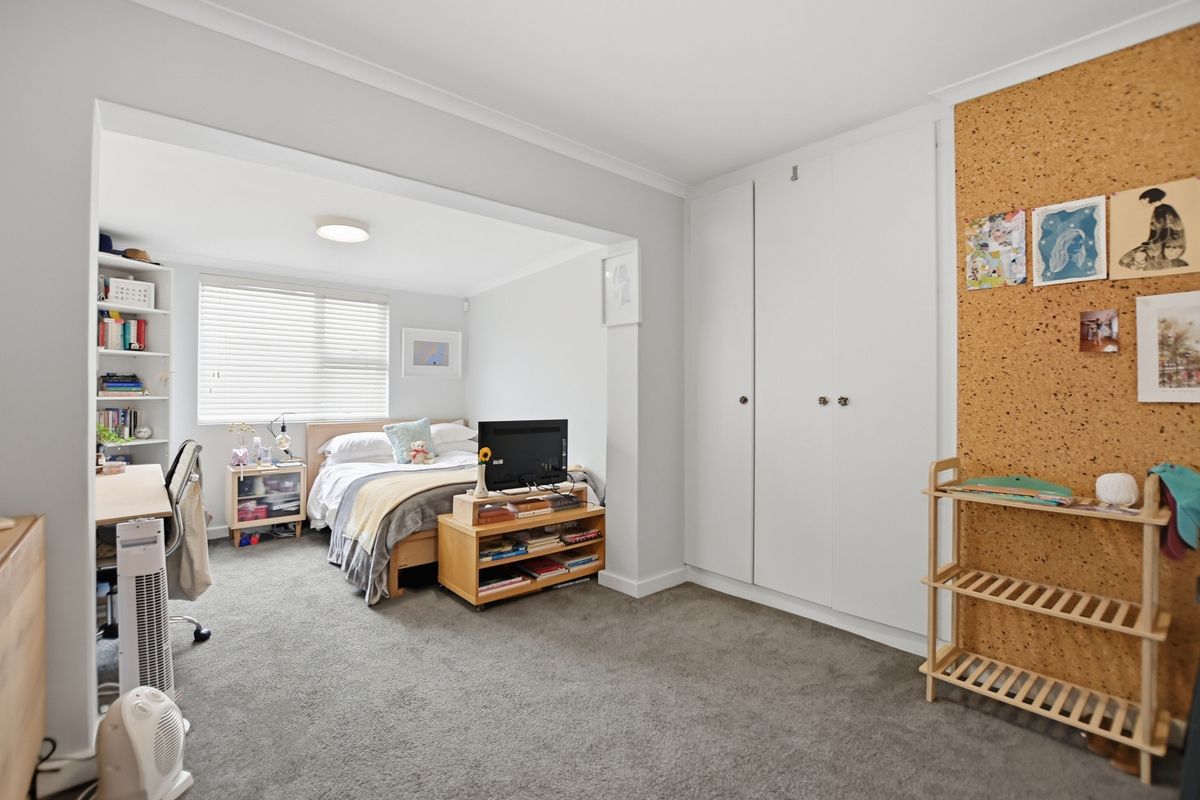 A spacious bedroom featuring built-in wardrobes, a recessed study nook, and neutral carpeting, offering a functional and comfortable living space.