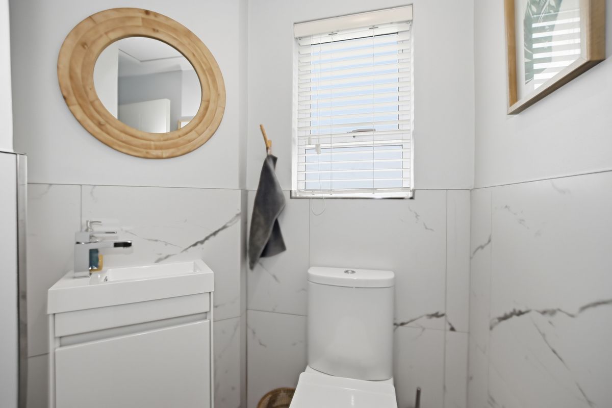A modern guest bathroom featuring marble-look wall tiles, a sleek vanity with a basin, and a contemporary toilet.