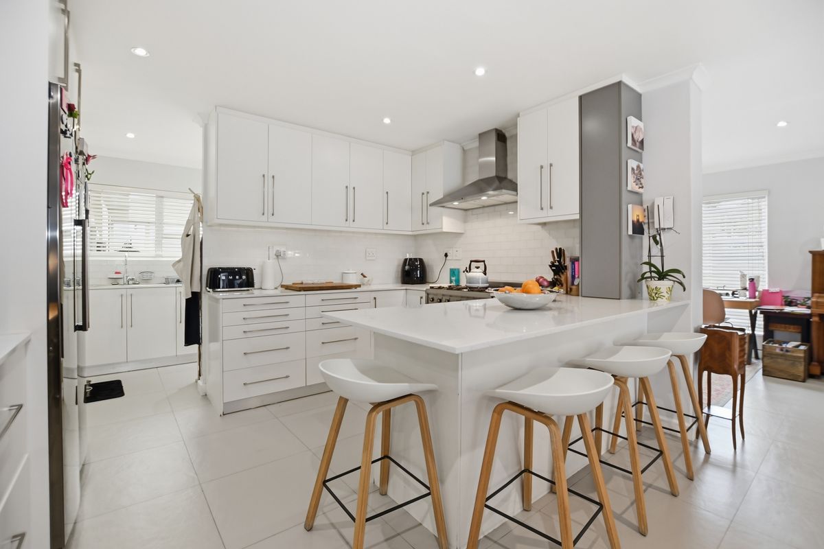 Modern kitchen featuring white cabinetry, stone countertops, a central island with breakfast bar seating, and a stainless steel extractor fan.