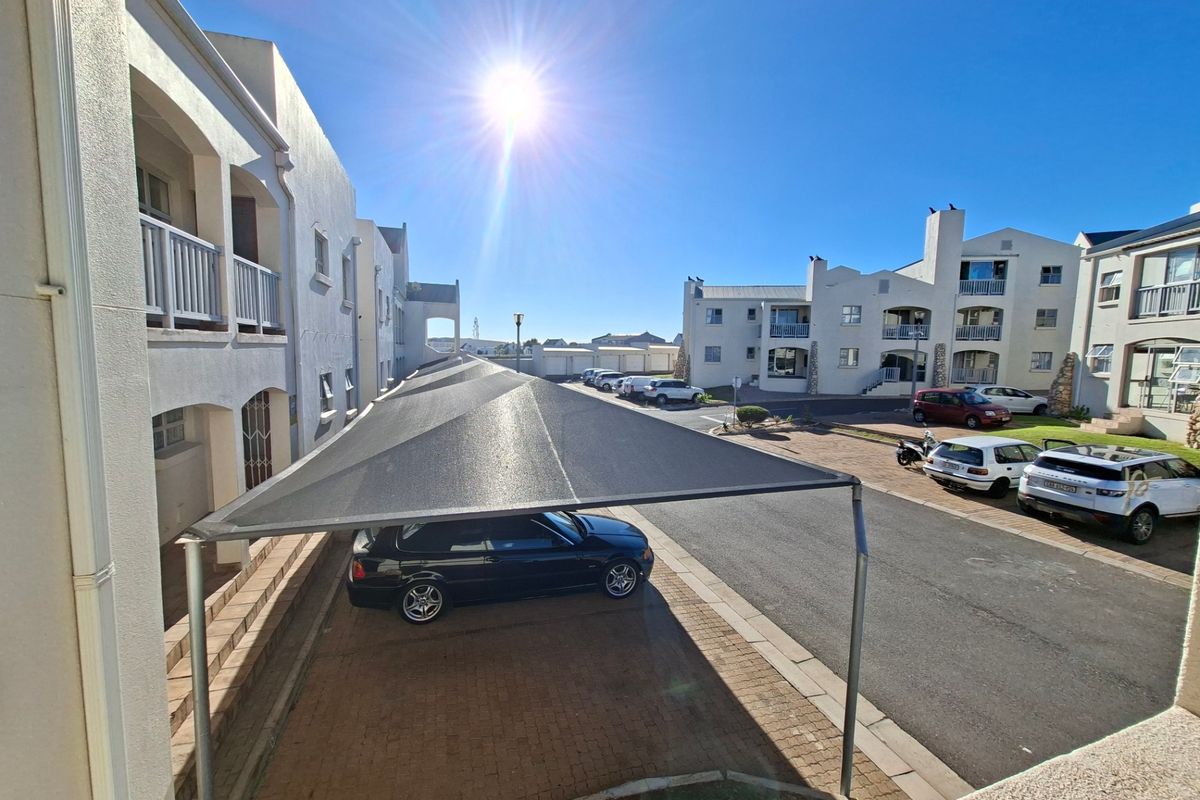 View of the apartment complex parking area featuring covered shade-cloth carports and paved driveway access.