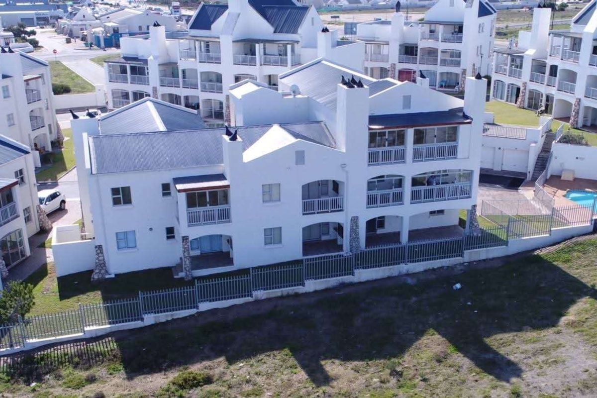 Aerial view of a multi-story apartment complex featuring white facades, metal roofing, and private balconies within a residential estate setting.