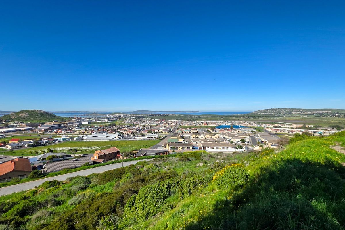 A wide-angle elevated view overlooking the surrounding residential neighborhood, coastal landscape, and distant hills under a clear blue sky.